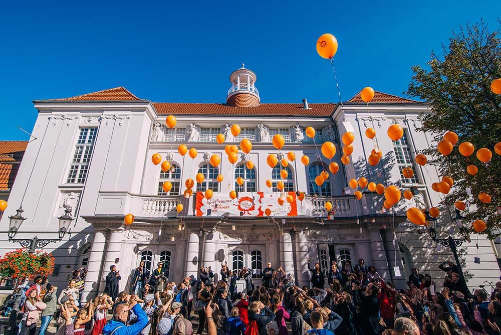 Viele Menschen stehen vor dem Stadttheater Minden und lassen orangene Ballons steigen