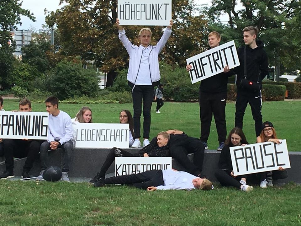 Mehrere junge Leute stehen, sitzen oder liegen auf einer Sitzmauer und halten Schilder