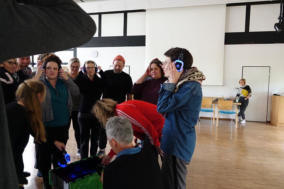 Mehrere Menschen in einem Raum haben Kopfhörer auf und hören sich etwas an