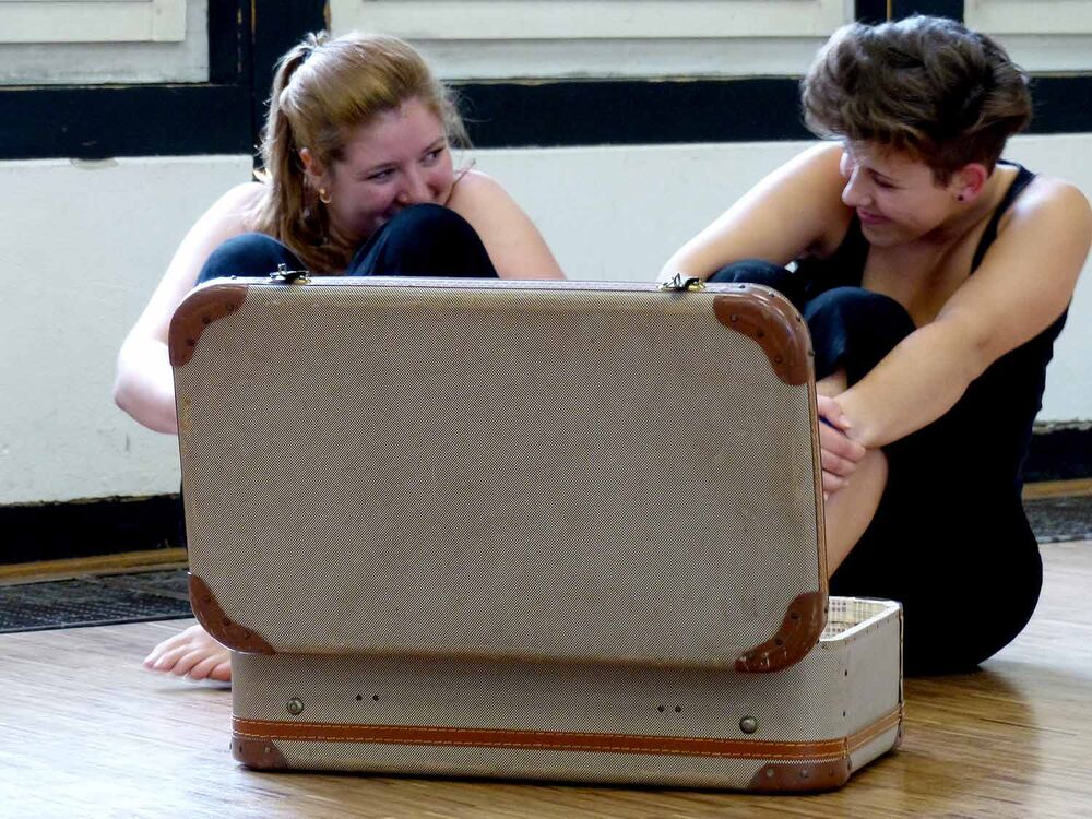 2 junge Frauen sitzen amüsiert vor einem offenen Koffer.